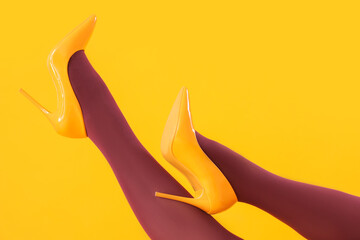 Female legs in black tights and high heels on yellow background