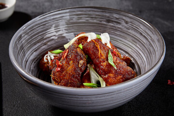 Fried Buffalo wings in Asian style on a black background. Sliced greens on wings, spices, and chopsticks in the background
