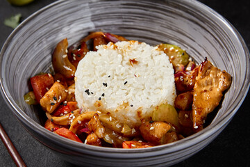 A grey bowl filled with Chinese-style seafood rice presented on a black background. Accompanied by chopsticks and sesame seeds scattered around the table