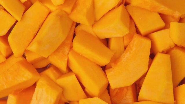 Slices of fresh pumpkin chunks background. Yellow Juicy pieces of pumpkin. Texture close up. Turning, rotation. Full frame with copy space for text, label. Food backdrop. Bright orange sliced pumpkin.