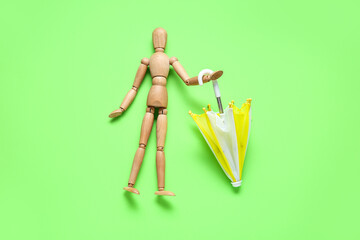 Creative composition with wooden mannequin and mini umbrella on green background
