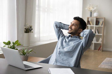 Positive dreamy Indian employee man thinking over career success, enjoying leisure, relaxation, work break at workplace, resting in office armchair, looking away, smiling, breathing fresh air