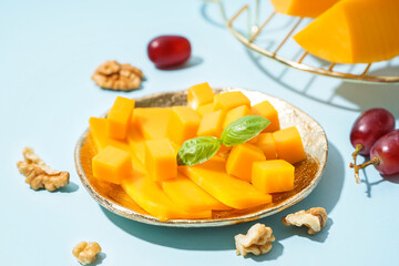Plate with pieces of tasty cheddar cheese, grapes and nuts on blue background, closeup