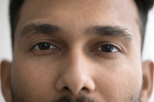 Upper face of handsome young Indian man with thick black eyebrows looking at camera. Front view, cropped clos ep shot. Male model promoting eye care, eyesight, vision checkup