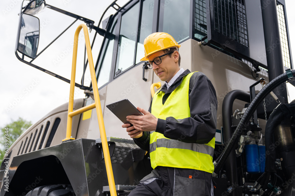Poster Engineer with tablet computer stands on the stairs to the cab of a truck	