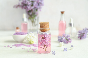 Fototapeta na wymiar Bottles of cosmetic oil with beautiful lilac flowers and sea salt on white table