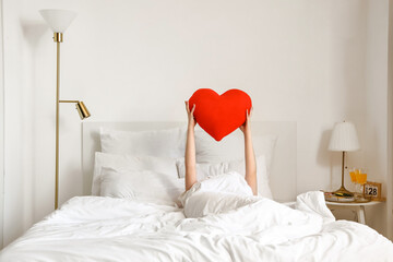 Morning of young woman with heart shaped pillow in bed