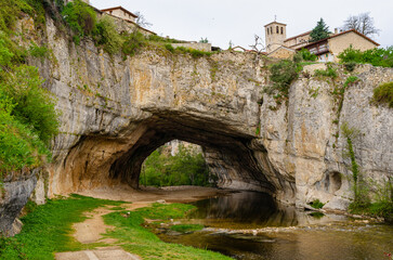 Fototapeta na wymiar Natural bridge in the village Puentedey formed by a flowing river. Tunnel within rock underneath a village in Spain. 