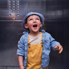 Happy baby rides in the elevator of an apartment building with buttons on the wall. A child in an...