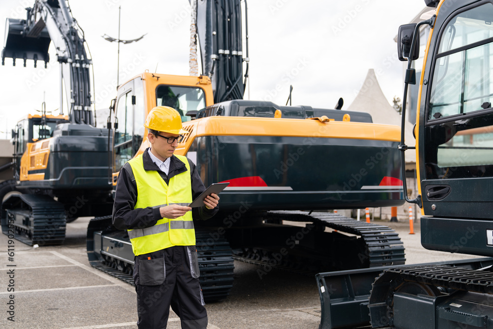 Aufkleber engineer in a helmet with a digital tablet stands next to construction excavators