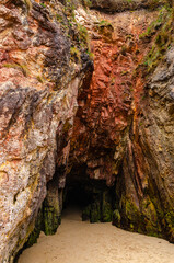 A detail of a cave entrance on a sandy beach. Walk into deep dark rock hole.