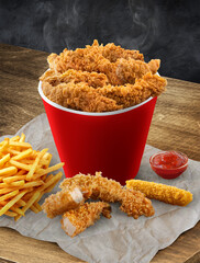 Fried chicken bucket  on a table, with fries, and crispy golden pieces of chicken meal, with Mozzarella stick on the surface of the wooden table with red sauce perfect poster
