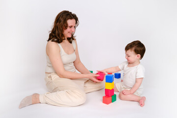 Happy baby with mother play educational toys on studio white background. Portrait of a smiling child with mom and playing while sitting on the floor. Kid about two years old (one year nine months)