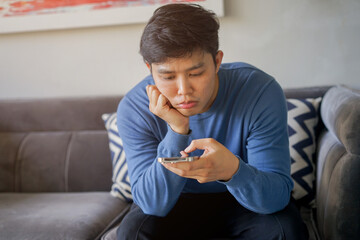 close up asian teenager man feeling bored while playing smartphone at house for teenage and...