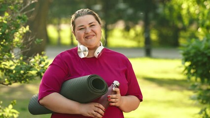 Plus size woman with exercise mat looking at camera