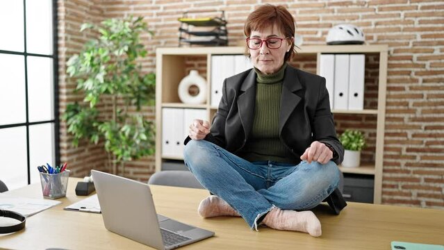 Mature hispanic woman business worker doing yoga meditation on the table at office