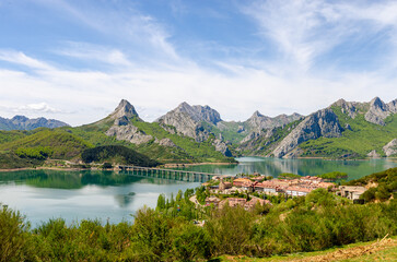 Mountain peaks in Spain national park Picos de Europa - Riano with a village on a lake with bridge. Beautiful green hill tops full of trees and nature.