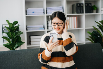 Smiling girl relaxing at home, she is playing music using smartphone tablet, laptop, and wearing white headphones. on sofa .