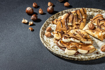 Homemade thin crepes with chocolate spread, banana and hazelnuts. breakfast or dessert. banner, menu, recipe place for text, top view