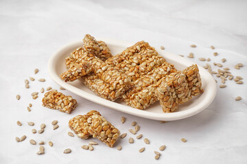 Plate with tasty pieces of kozinaki and sunflower seeds on white background