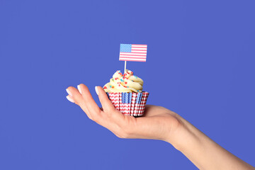 Female hand with tasty patriotic cupcake and USA flag near blue wall. American Independence Day
