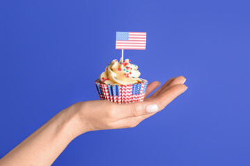 Female hand with tasty patriotic cupcake and USA flag near blue wall. American Independence Day