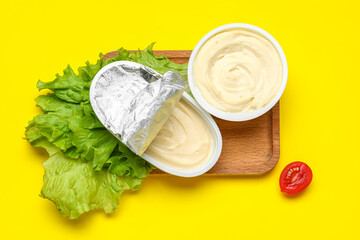 Wooden board with box of processed cheese and vegetables on yellow background