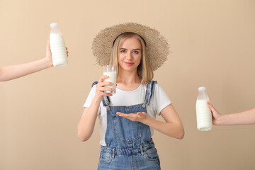 Female farmer with glass of milk and hands holding bottles on beige background