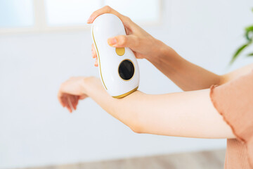 A woman using an epilator to remove unwanted arm hair at home.