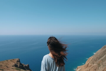 Fototapeta na wymiar Woman with dark hair stands on a top cliff over blue sea view while wind rear view