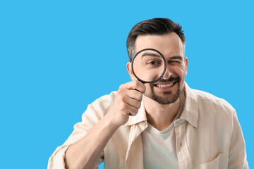 Handsome man with magnifier on blue background