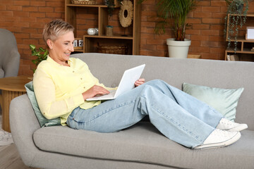 Fototapeta na wymiar Mature female freelancer working with laptop on sofa at home