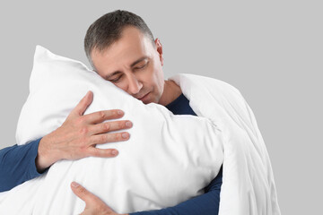 Mature man with soft pillow and blanket on grey background, closeup