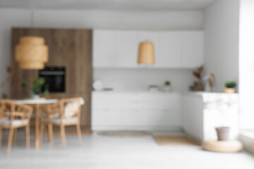Fototapeta na wymiar Interior of light kitchen with built-in oven, table, chairs and white counters, blurred view