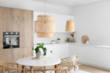 Interior of light kitchen with built-in oven, table, chairs and white counters, blurred view