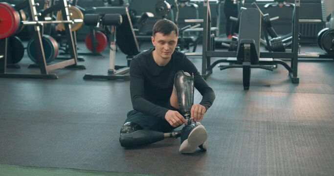 smiling sportsman going to train in a gym, Disabled man athlete is ready for training with leg prosthesis. Paralympic Sport Concept. guy talking with friend sitting on floor