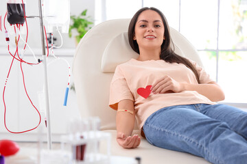 Female blood donor with applied medical patch and paper heart in clinic