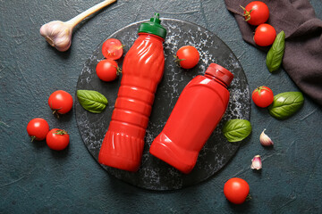 Board with bottles of ketchup and tomatoes on dark background