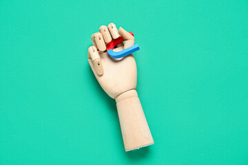 Wooden hand with horseshoe shaped mini magnet on green background
