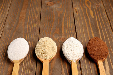 Wooden spoons with different types of flour and cacao on brown wooden background
