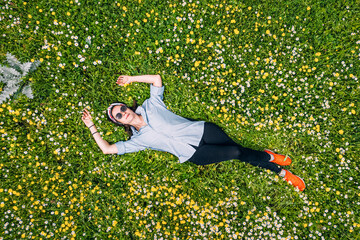 Aerial view of a happy woman lying on a grass with wildflowers in park