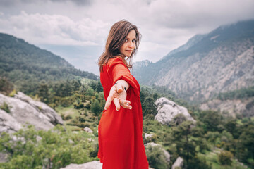 Follow me - a girl in a red dress on top of a cliff admiring the view of a mountain gorge