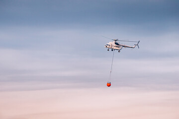 Fototapeta na wymiar a firefighter emergency helicopter flying to the accident area with a basket with water against sky background
