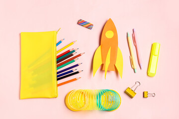Paper rocket with pencil case and different stationery on pink background