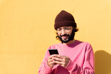 Fototapeta premium smiling young man using mobile phone in a yellow background, concept of technology of communication and modern lifestyle, copy space for text