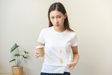 Cloth stain, disappointment asian young woman clumsy with hot coffee, tea stains on shirt, hand show making spill drop on white t-shirt, spot dirty or smudge on clothes at home, isolated on background - obrazy, fototapety, plakaty