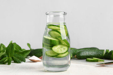 Bottle of infused water with cucumber slices on white table