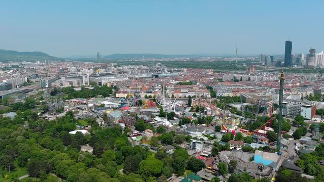 Aerial city view of Vienna, Austria, from above at Prater amusement park. Flying by iconic fairy wheel and other amusement rides ft beautiful Vienna skyline in background on a sunny summer day 4K