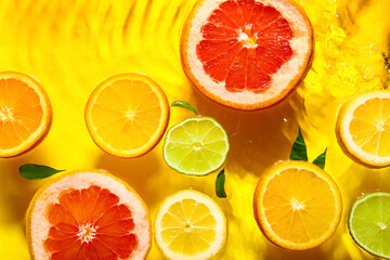 Different citrus fruit slices and leaves in water on yellow background