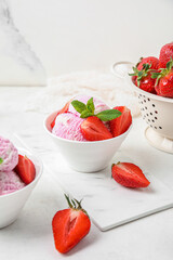 Bowls of strawberry ice cream with berries and mint on white table near grunge wall